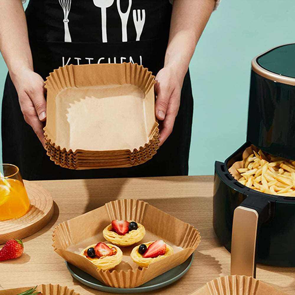 Stack of brown square air fryer disposable parchment paper liners held by person near air fryer and plate with desserts